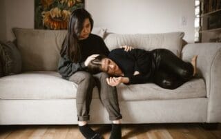 Two women sit together on a sofa, one offering empathetic support to the other in a moment of emotional comfort.
